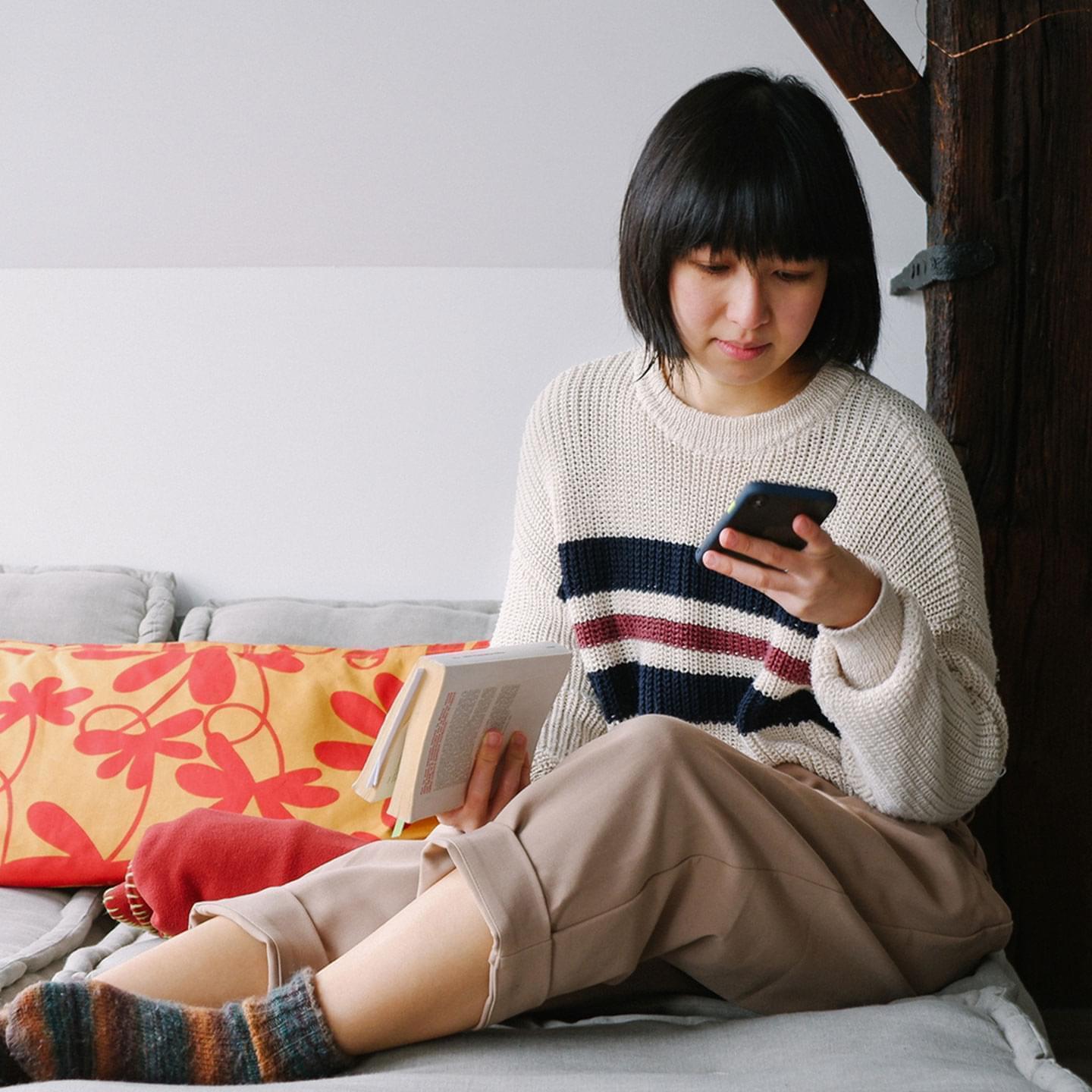 A picture of a person holding a book and a mobile phone, tracking reading progress in a mobile app