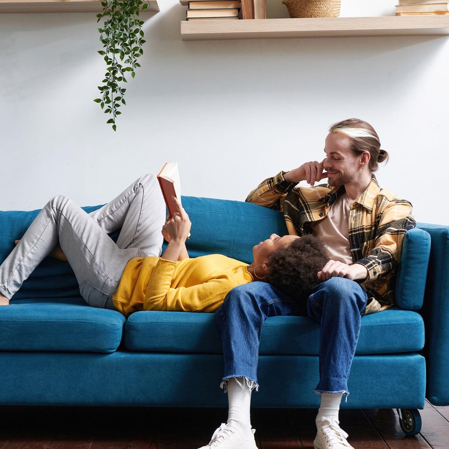 A picture of a young couple sitting on a blue couch reading a book together